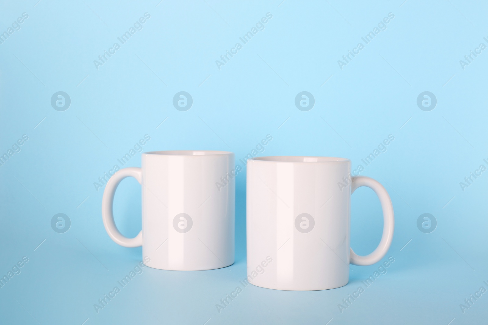 Blank white ceramic mugs on light blue background Photo of Blank white ceramic mugs on light blue background