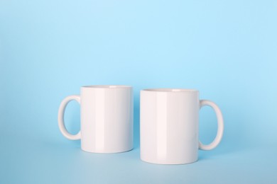 Photo of Blank white ceramic mugs on light blue background