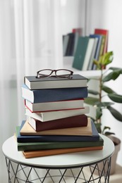 Photo of Stack of many different books and glasses on coffee table indoors