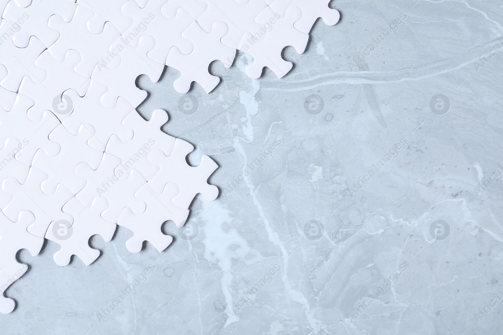 Photo of Blank white puzzle pieces on light grey marble background, flat lay. Space for text