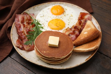 Tasty pancakes with fried eggs and bacon on wooden table, closeup