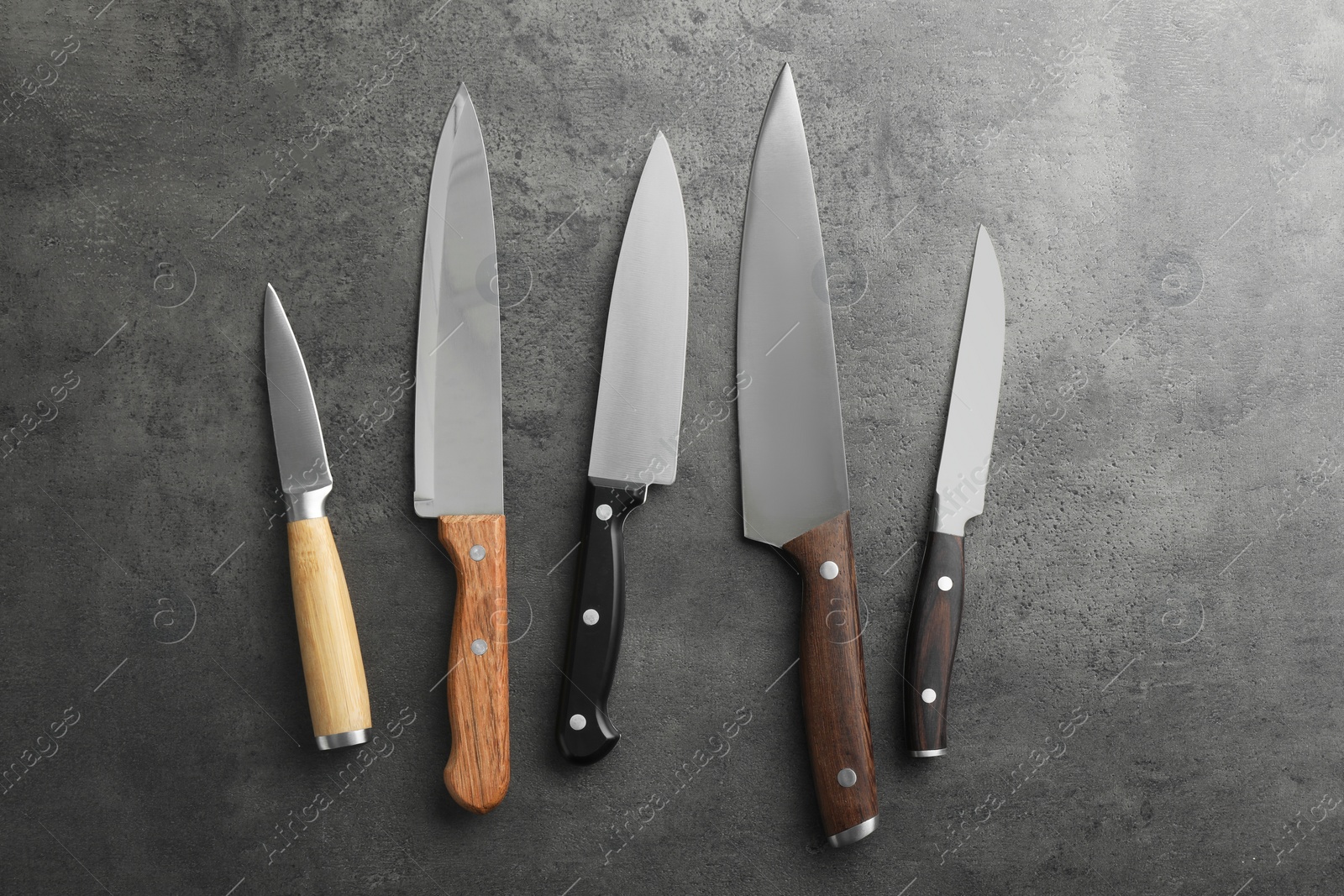 Photo of Many different knives on grey textured table, flat lay