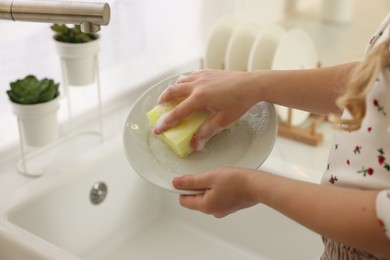 Photo of Little girl washing plate above sink, closeup