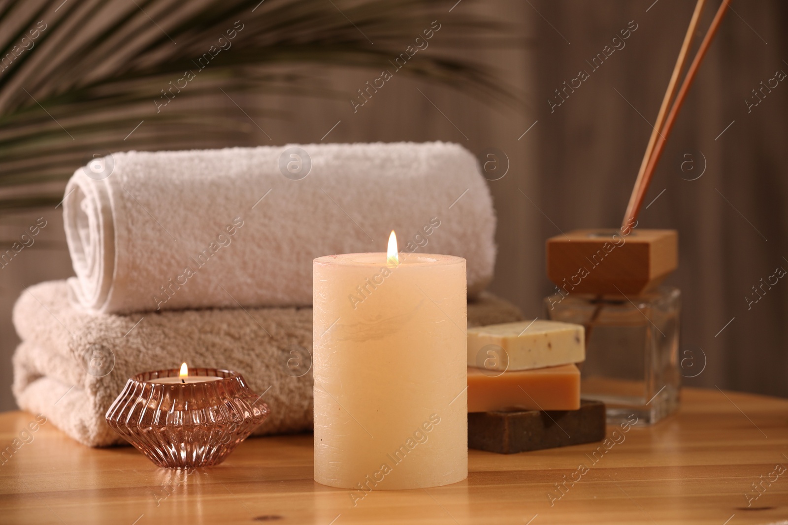 Photo of Spa composition. Burning candles, towels, soap and reed air freshener on wooden table, closeup