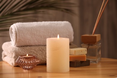 Spa composition. Burning candles, towels, soap and reed air freshener on wooden table, closeup