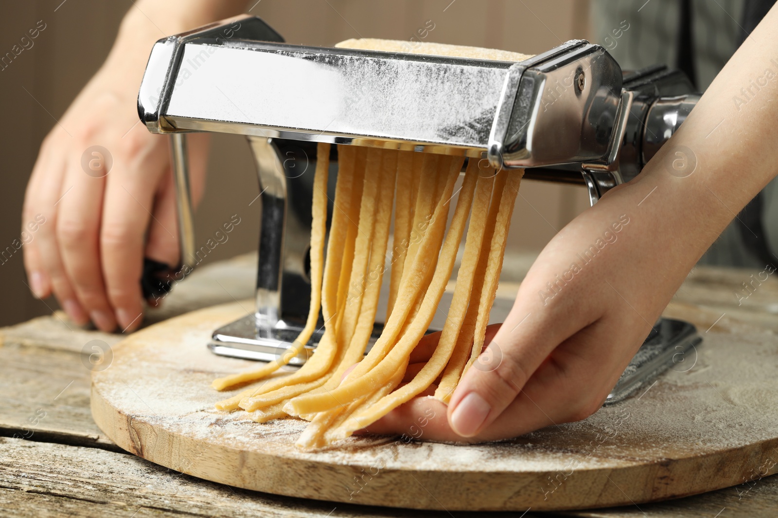Photo of Woman making homemade noodles with pasta maker at wooden table, closeup