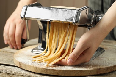 Woman making homemade noodles with pasta maker at wooden table, closeup