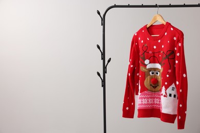 Photo of Rack with Christmas sweater on light background, space for text