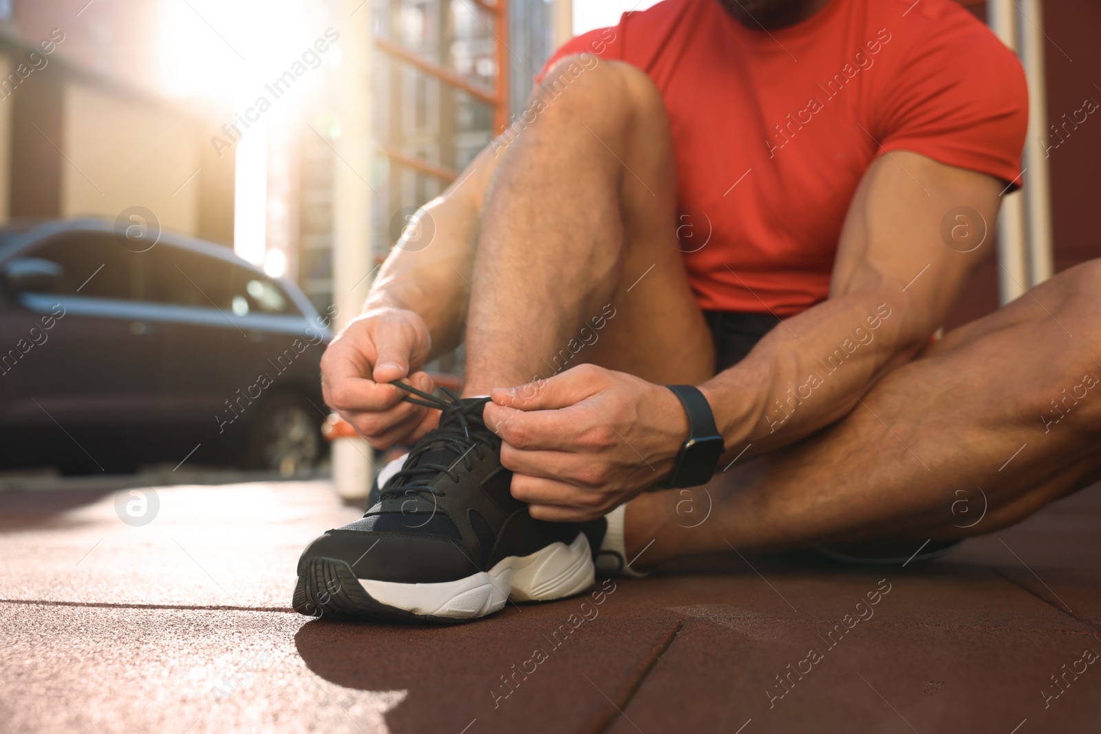 Photo of Man tying shoelaces before training at outdoor gym on sunny day, closeup