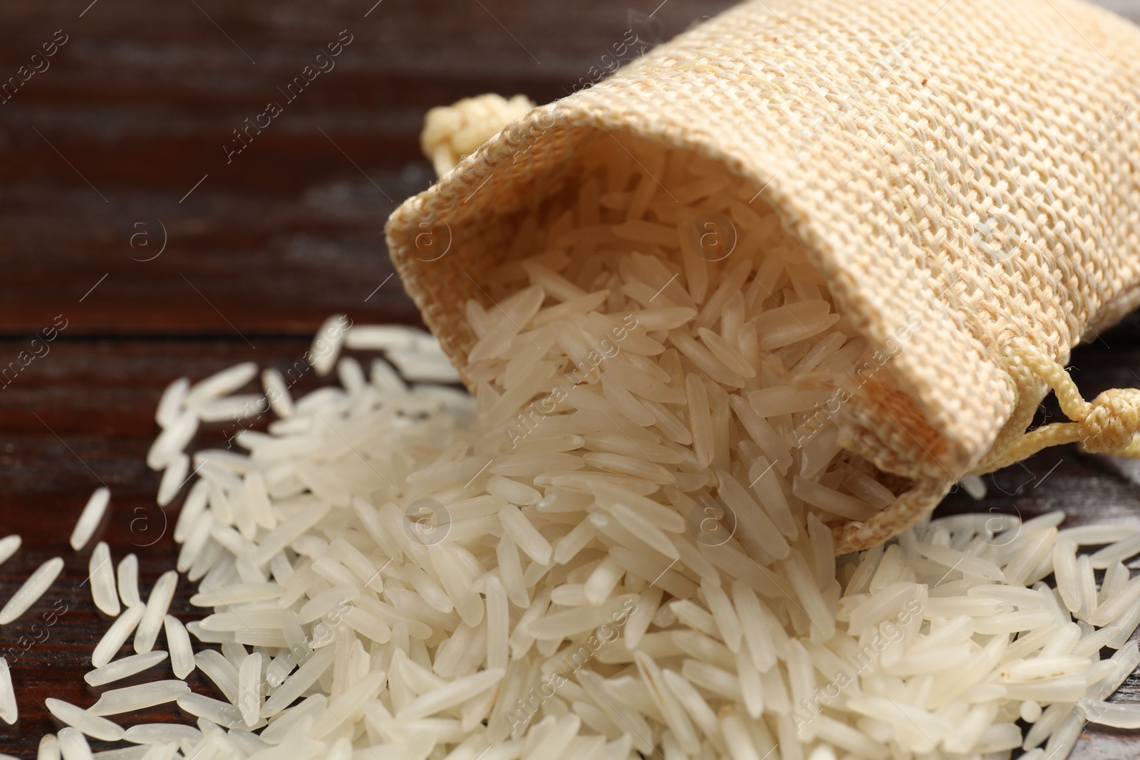 Photo of Raw basmati rice and bag on wooden table, closeup