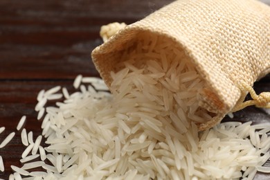 Photo of Raw basmati rice and bag on wooden table, closeup