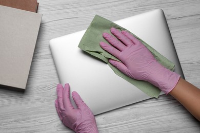 Photo of Woman wiping tablet with paper towel at white wooden table, top view