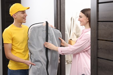 Photo of Dry-cleaning delivery. Happy courier giving garment cover with clothes to woman indoors