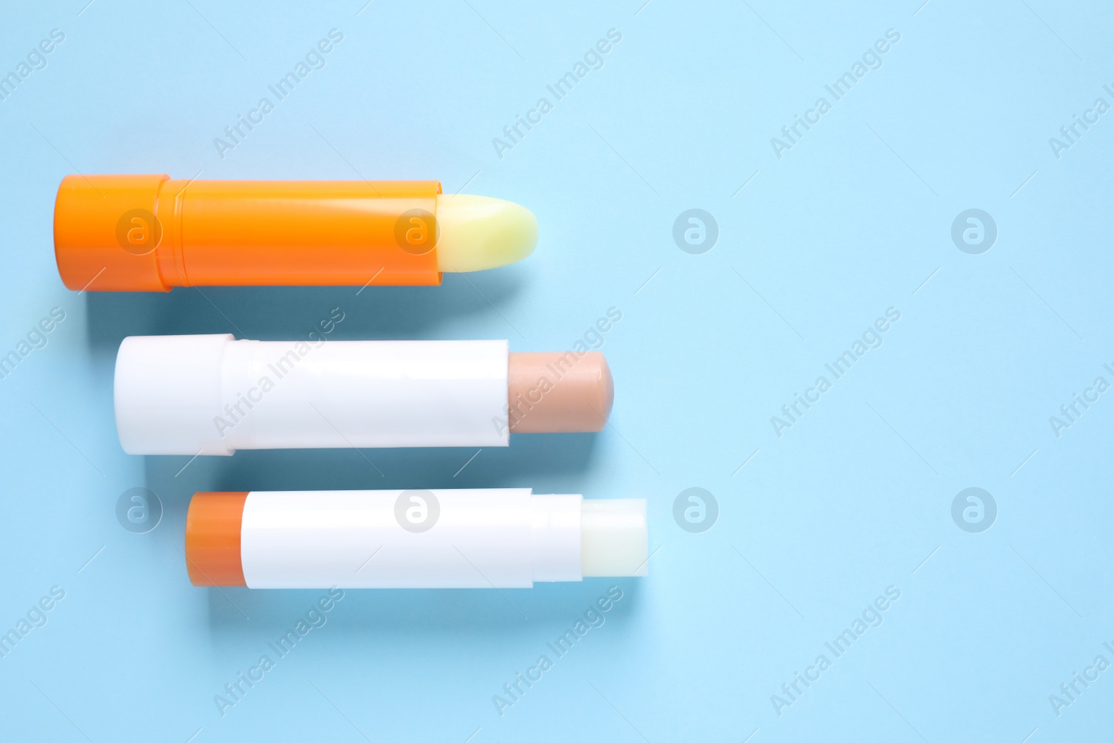 Photo of Hygienic lipsticks on light blue background, flat lay. Space for text