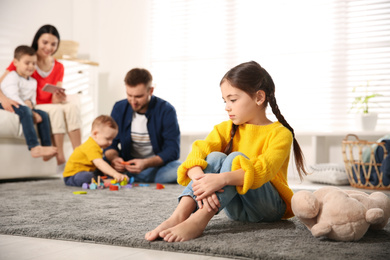 Photo of Unhappy little girl feeling jealous while parents spending time with other children at home