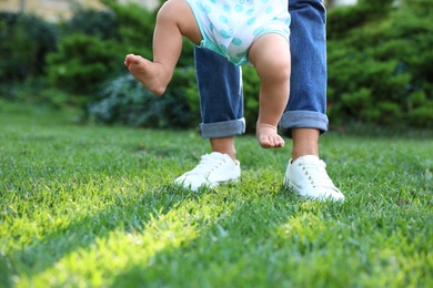 Cute little baby learning to walk with his nanny on green grass outdoors, closeup