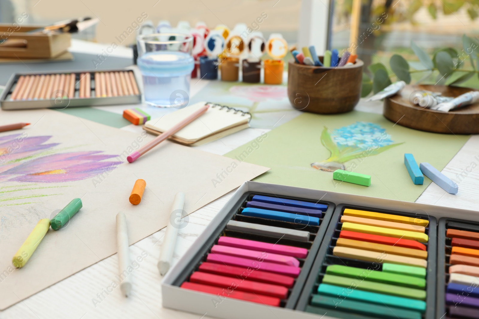 Photo of Artist's workplace with drawings, soft pastels and color pencils on table indoors