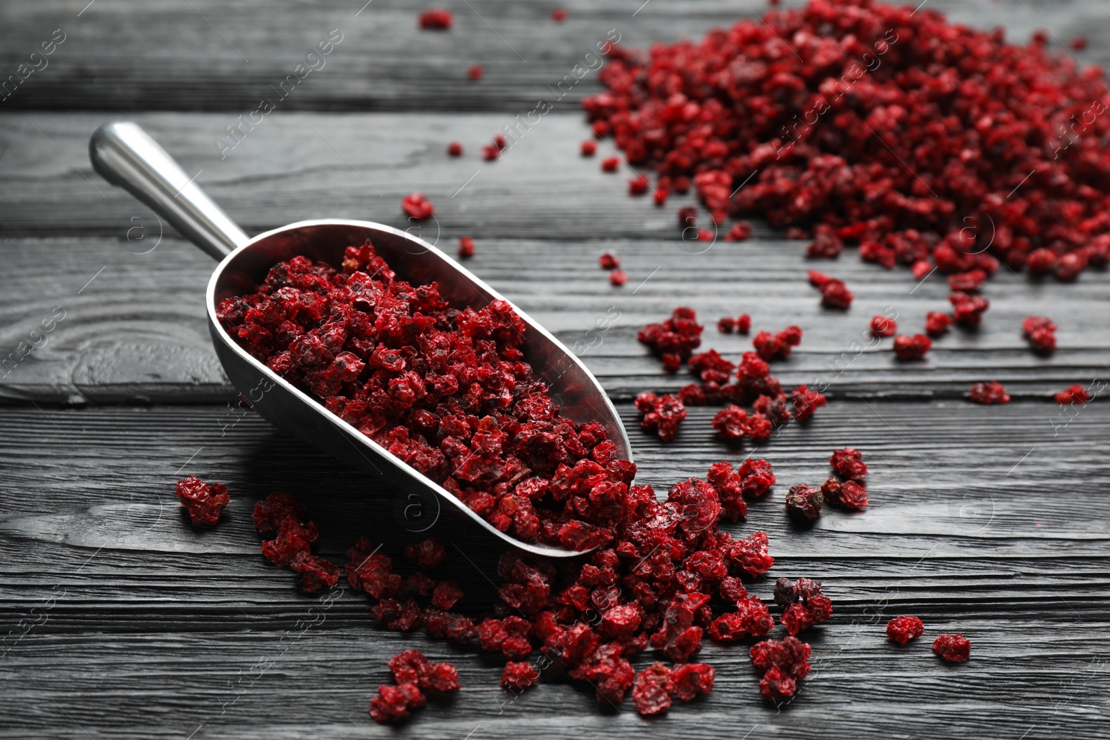 Photo of Metal scoop with dried red currant berries on black wooden table