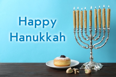 Happy Hanukkah. Silver menorah, dreidels and sufganiyah on wooden table against light blue background,