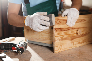 Professional carpenter polishing wooden drawer in workshop, closeup