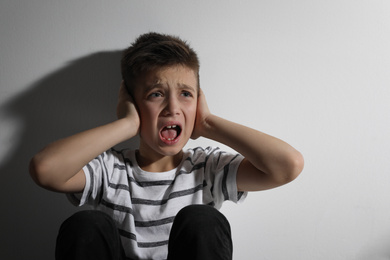 Photo of Scared little boy closing his ears near white wall. Domestic violence concept