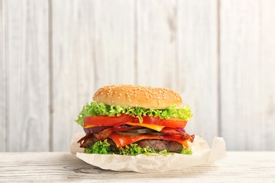 Photo of Tasty burger with bacon on table against wooden background. Space for text