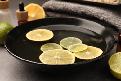 Photo of Bowl of essential oil and lemons on grey table, closeup. Aromatherapy treatment