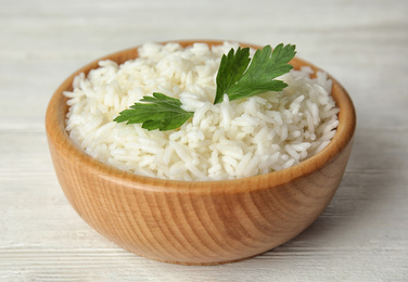 Bowl with tasty cooked rice and parsley on white wooden table, closeup