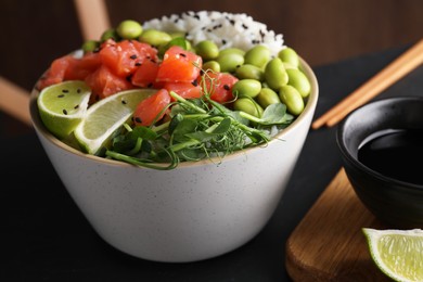 Photo of Delicious poke bowl with lime, fish and edamame beans on black table, closeup