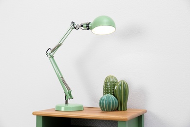 Photo of Stylish lamp and decorative cacti on table against white background