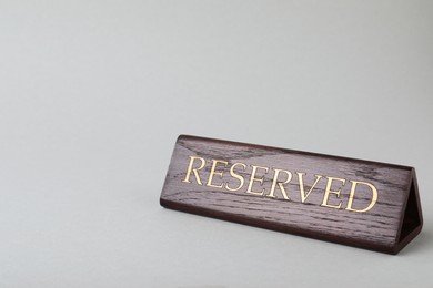 Photo of Elegant wooden sign RESERVED on light grey background, space for text. Table setting element