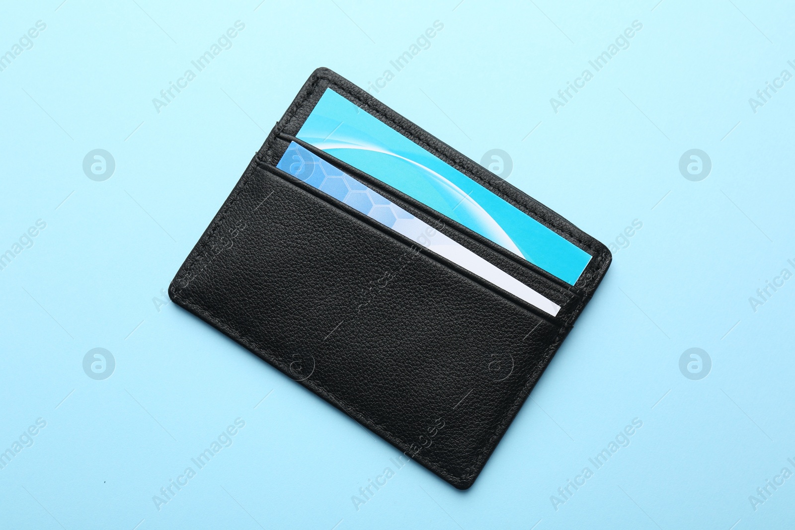 Photo of Leather business card holder with cards on light blue background, top view