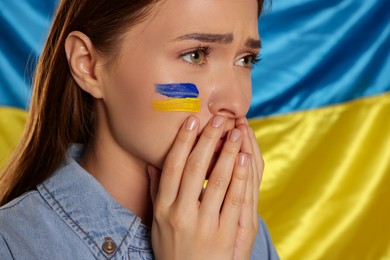 Photo of Sad young woman with clasped hands near Ukrainian flag, closeup. Space for text