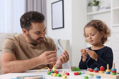 Photo of Motor skills development. Father and daughter playing with wooden pieces and strings for threading activity at table indoors