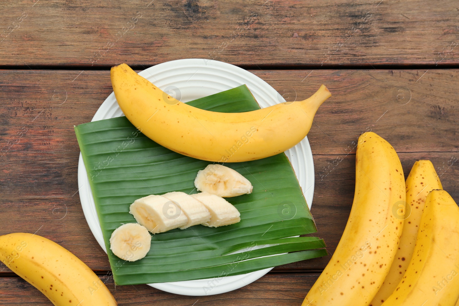 Photo of Delicious ripe bananas and fresh leaf on wooden table, above view