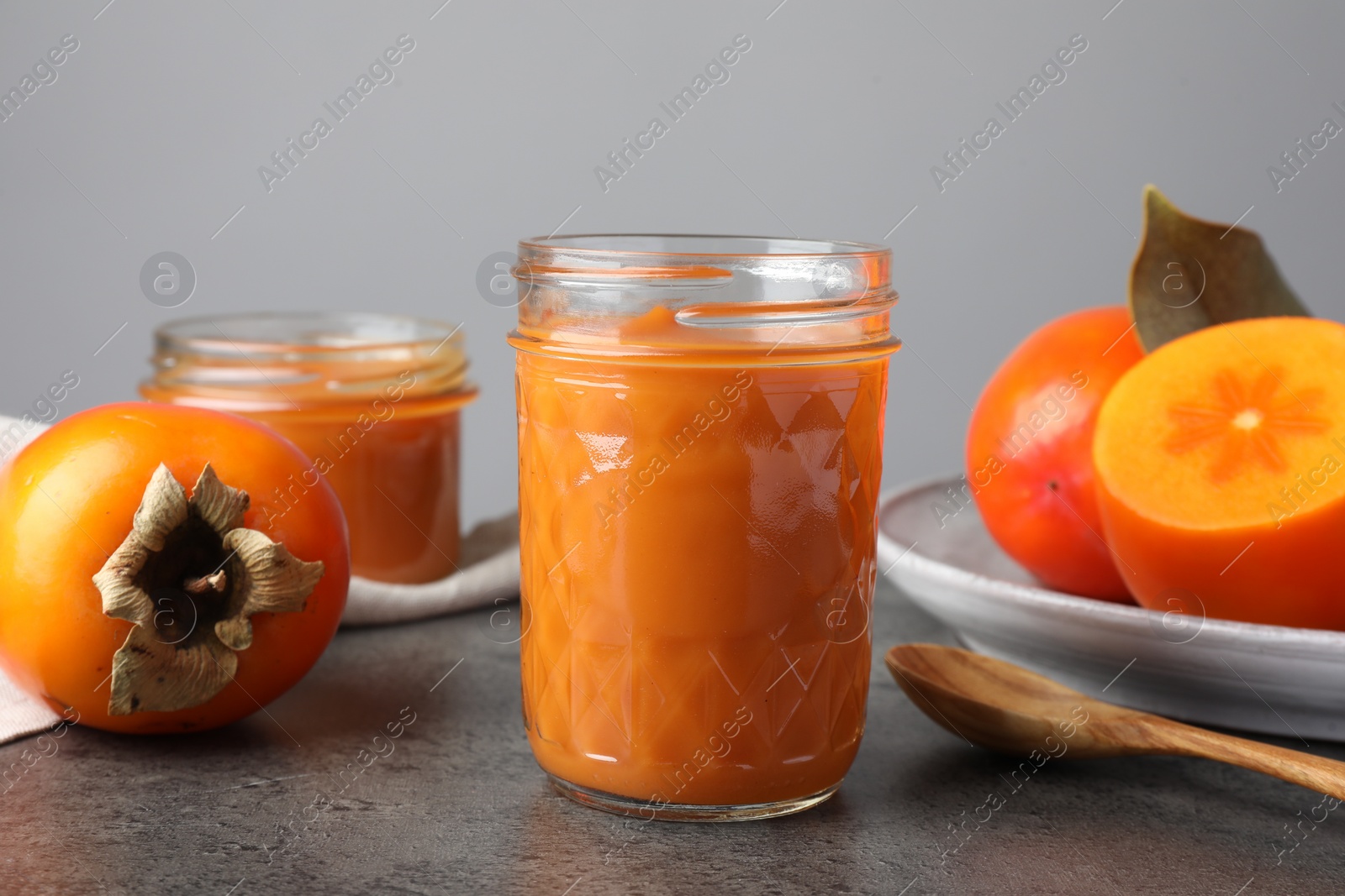 Photo of Delicious persimmon jam in glass jar served on gray table