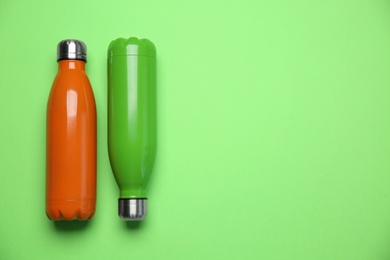 Photo of Different thermo bottles on green background, flat lay. Space for text