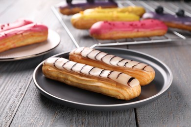 Photo of Different tasty glazed eclairs on wooden rustic table, closeup