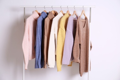 Photo of Warm sweaters hanging on rack against white background