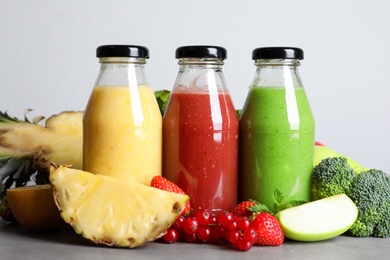 Bottles of delicious juices and fresh fruits on grey table