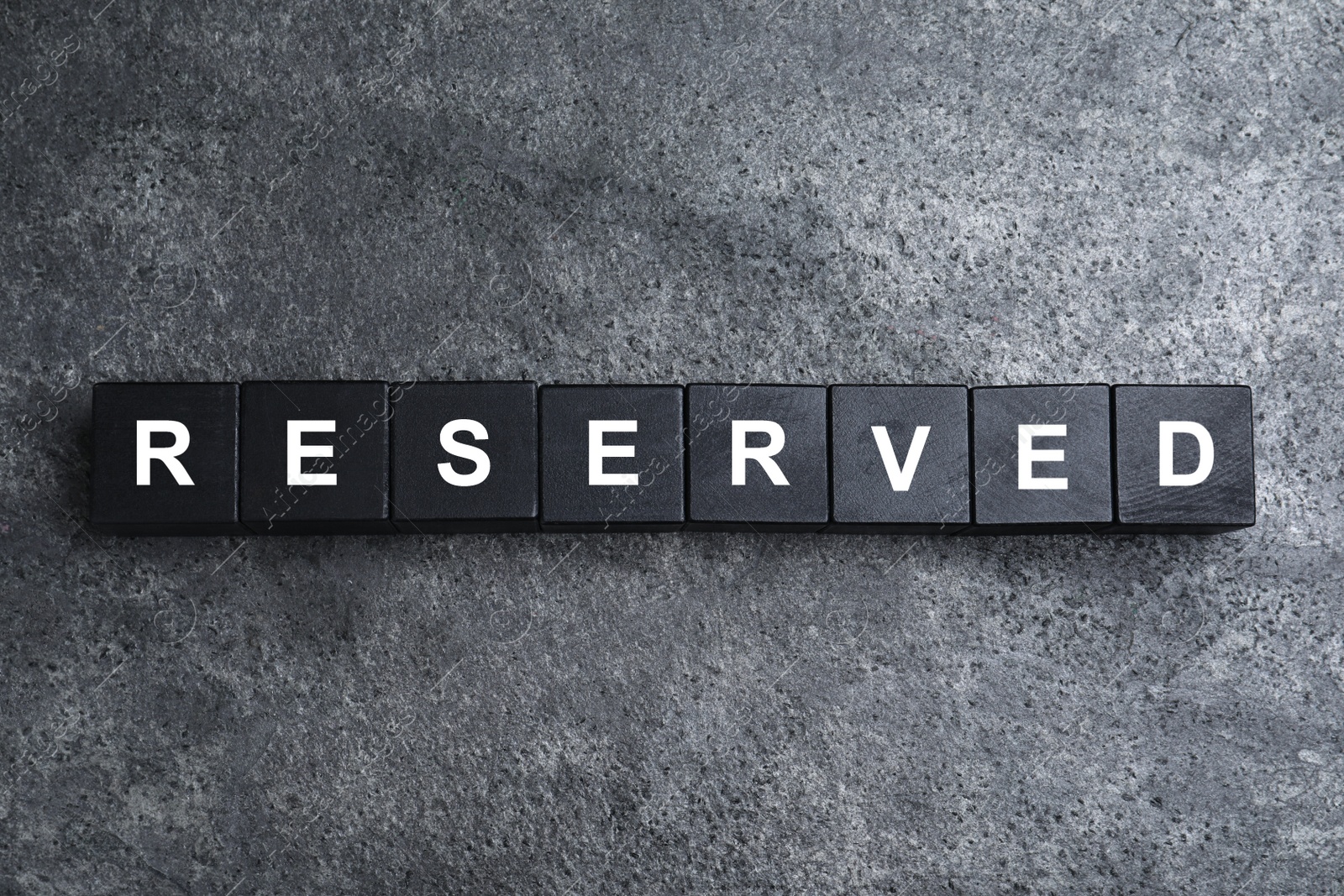 Photo of Word RESERVED made with cubes on grey surface, top view. Table setting element