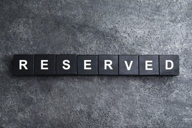 Word RESERVED made with cubes on grey surface, top view. Table setting element