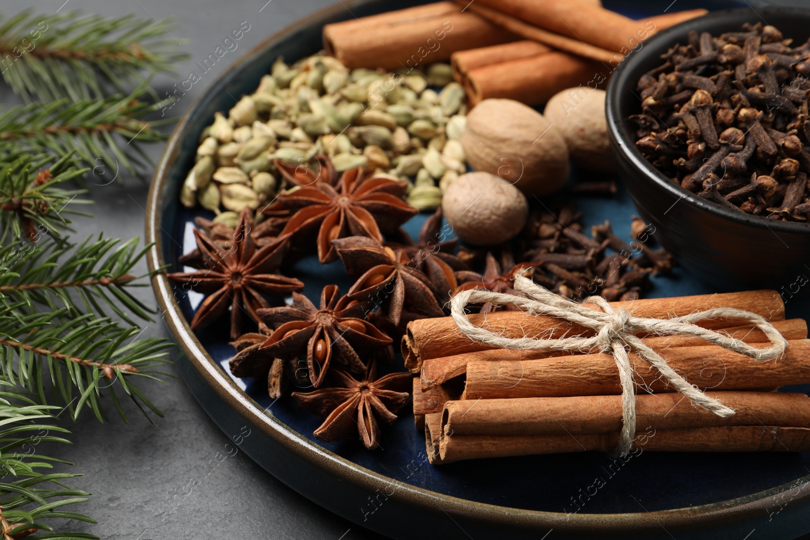 Photo of Dishware with different spices, nuts and fir branches on gray table, closeup