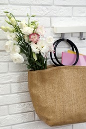 Photo of Stylish beach bag with beautiful bouquet and magazines hanging on hook rack indoors