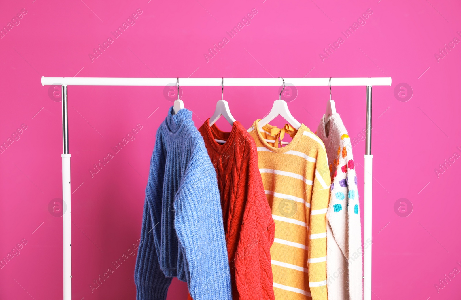 Photo of Collection of warm sweaters hanging on rack against color background