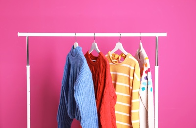 Collection of warm sweaters hanging on rack against color background