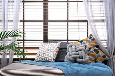 Plaid and pillows on bed near window indoors. Idea for interior design