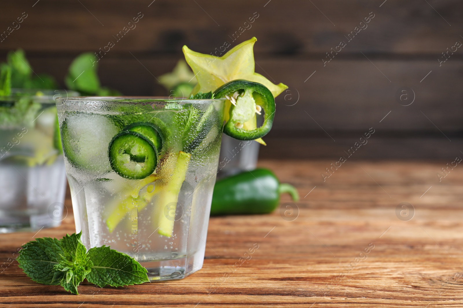 Photo of Spicy cocktail with jalapeno, carambola and mint on wooden table. Space for text