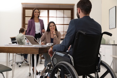 Photo of Young man in wheelchair with colleagues at workplace