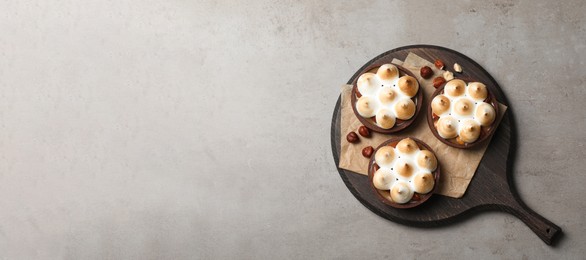 Photo of Delicious salted caramel chocolate tarts with meringue and hazelnuts on grey table, top view. Space for text